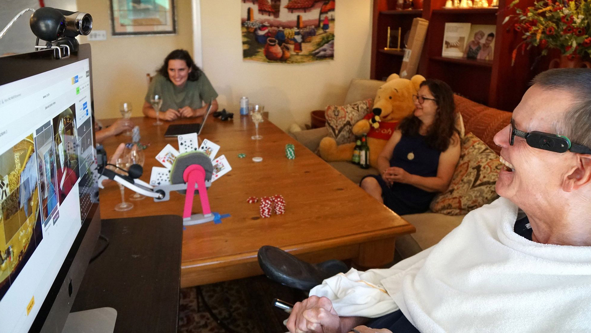 Evans in the foreground with computer screen. A table with playing cards separates him from two other people in the room