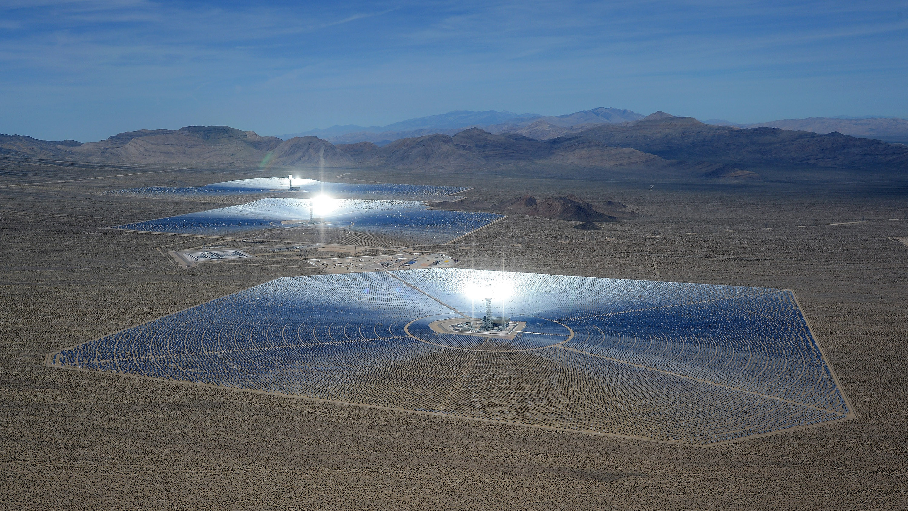 an aerial view of the Ivanpah Solar Electric Generating System in the desert with mountains in the distance